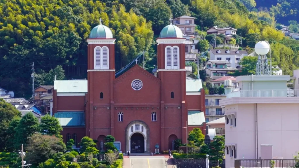 A red brick church with green domes surrounded by lush greenery and buildings in the background.